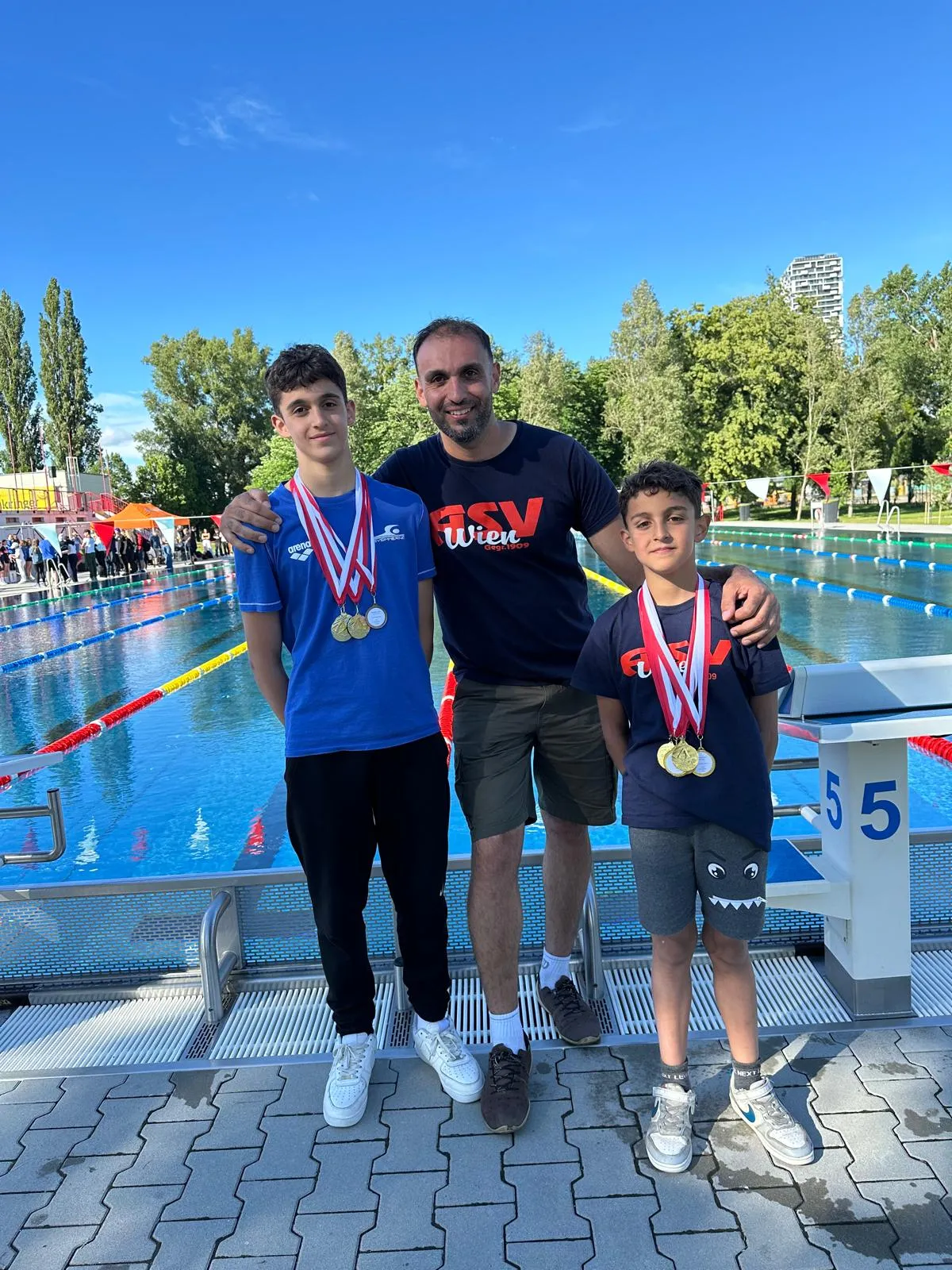 Trainer Ali and two proud swimmers showing of medals from outdoor pool competition