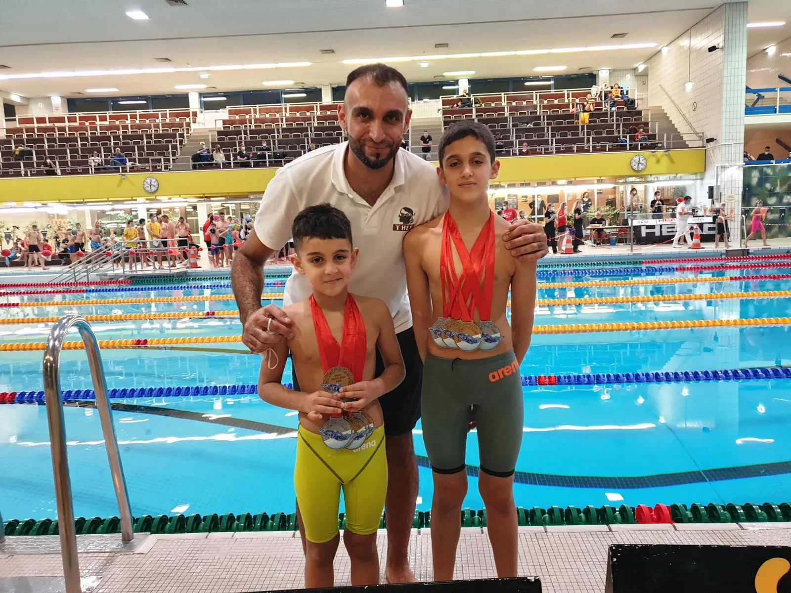 Trainer Ali and two proud swimmers showing of medals from indoor pool competition
