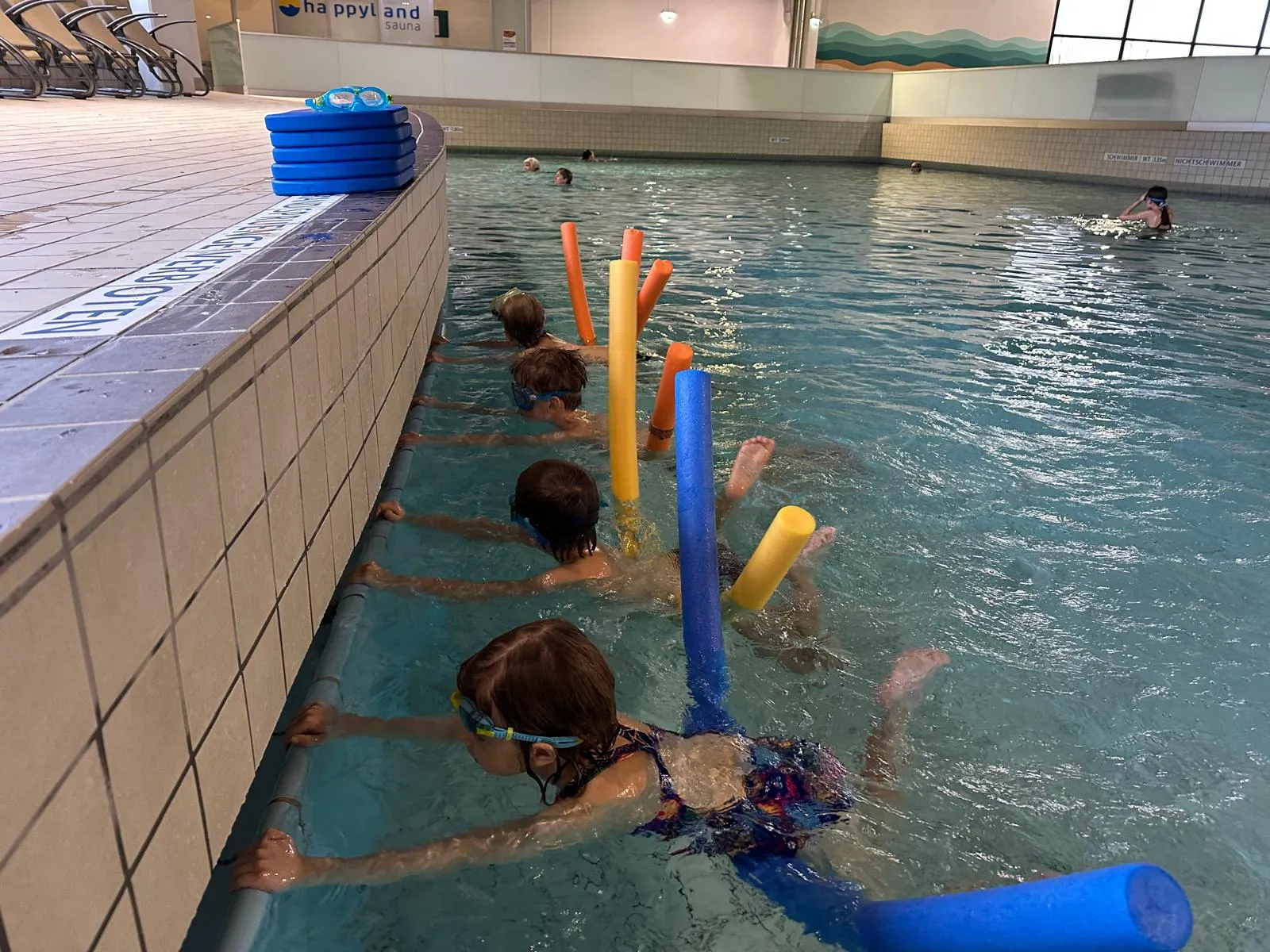 Children swimming lesson in pool using pool noodles